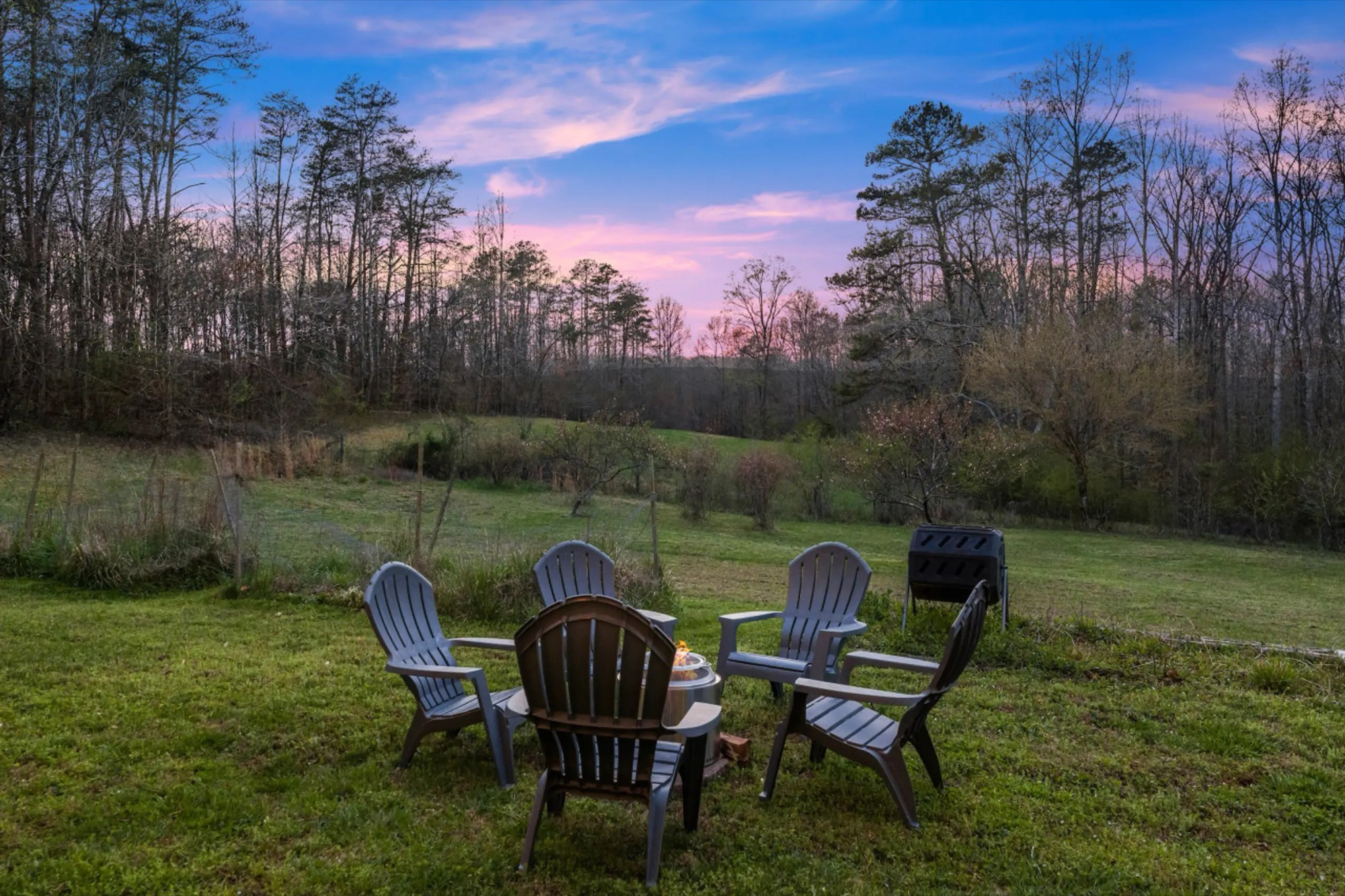Chairs around a fire pit in a field at dusk